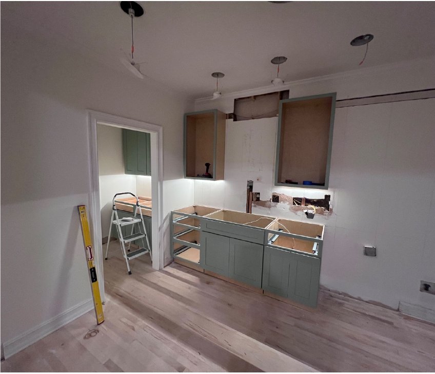 New muted green kitchen cabinets being installed during the renovation